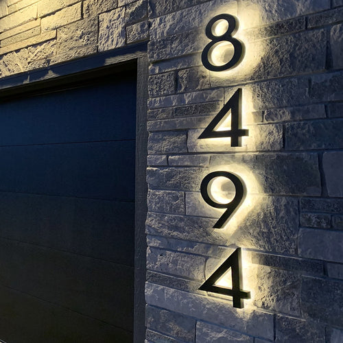 Black backlit LED house numbers 8494 lit on a stone wall