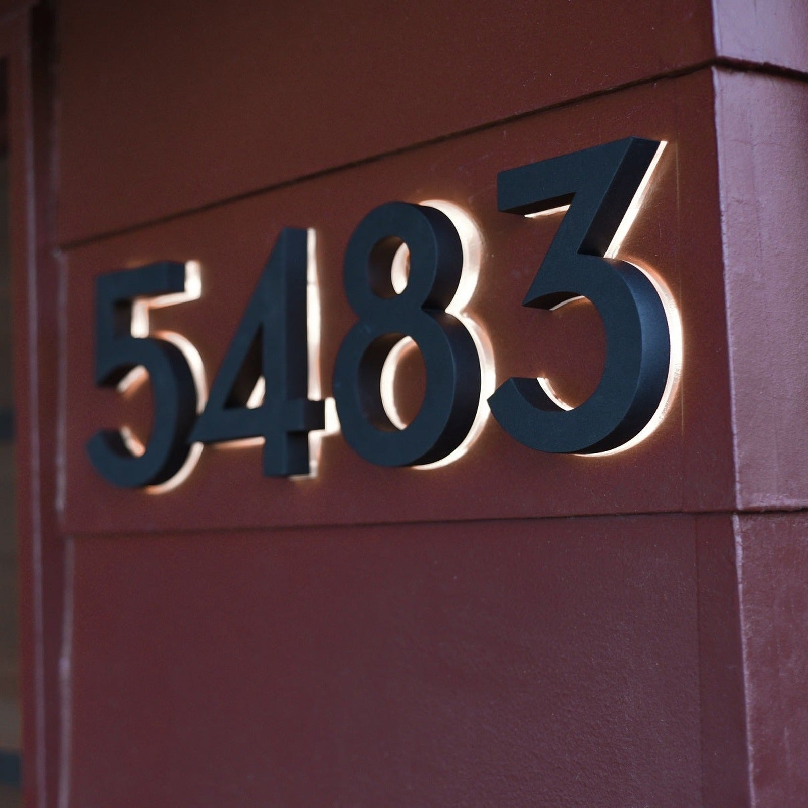 Black backlit LED house numbers 5483 lit on a red wall
