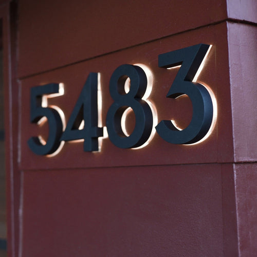 Black backlit LED house numbers 5483 lit on a red wall